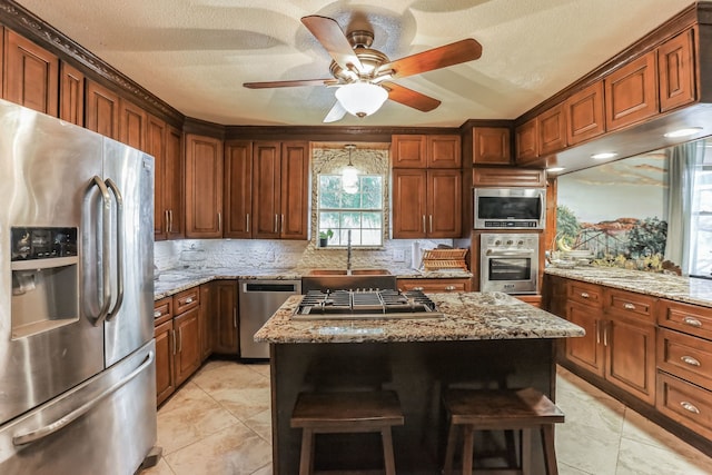 kitchen with light stone counters, appliances with stainless steel finishes, a center island, ceiling fan, and sink