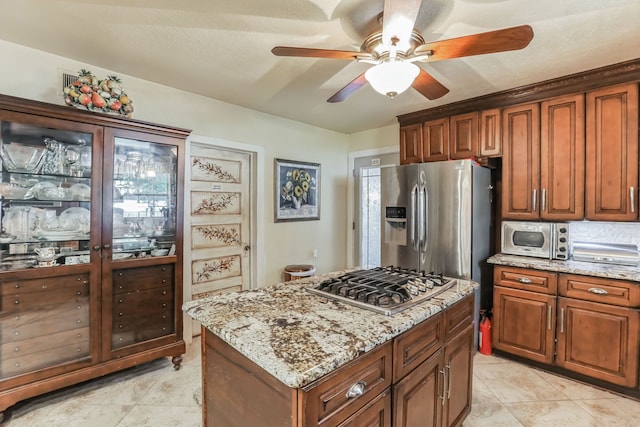 kitchen with a center island, light stone countertops, stainless steel appliances, light tile floors, and ceiling fan