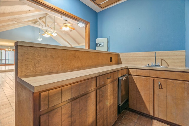 kitchen featuring dark tile patterned flooring, lofted ceiling with beams, brown cabinets, a sink, and ceiling fan with notable chandelier