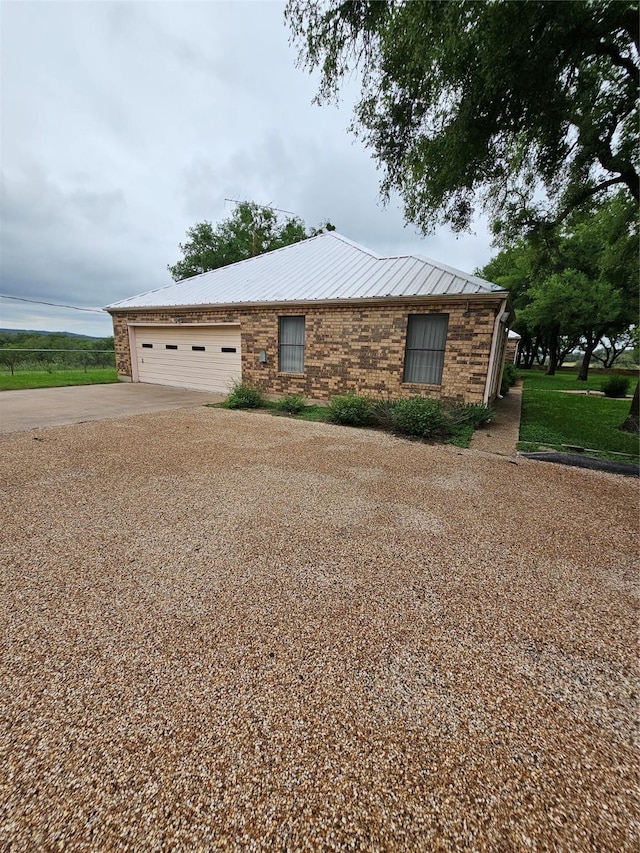 view of front of house with driveway, a garage, metal roof, and brick siding