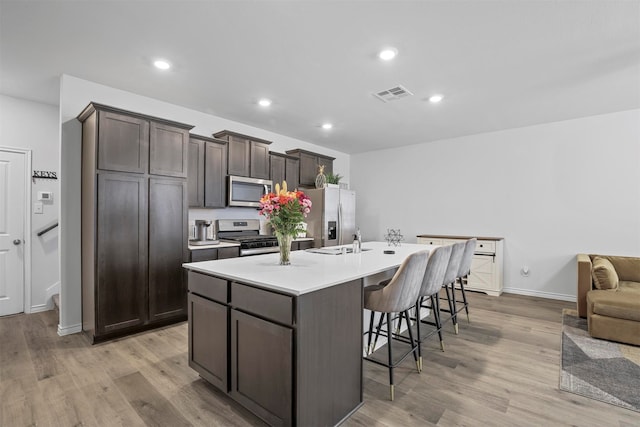 kitchen with light hardwood / wood-style flooring, dark brown cabinetry, stainless steel appliances, and a center island with sink