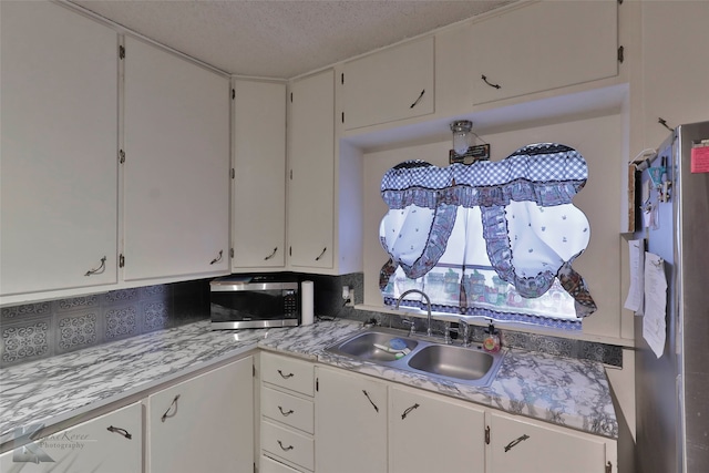 kitchen featuring backsplash, a textured ceiling, stainless steel appliances, sink, and white cabinetry