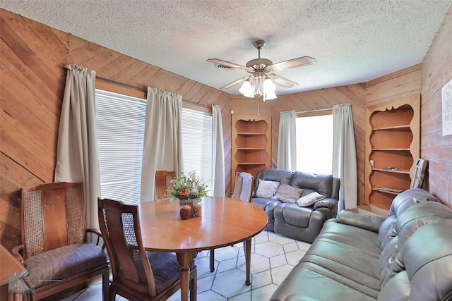 dining space featuring ceiling fan, a textured ceiling, and wooden walls