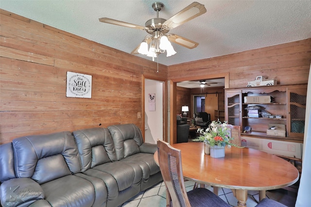 dining area with wood walls, light tile patterned flooring, a textured ceiling, and ceiling fan