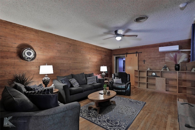 living room with a barn door, a wall mounted AC, wood walls, a textured ceiling, and hardwood / wood-style flooring