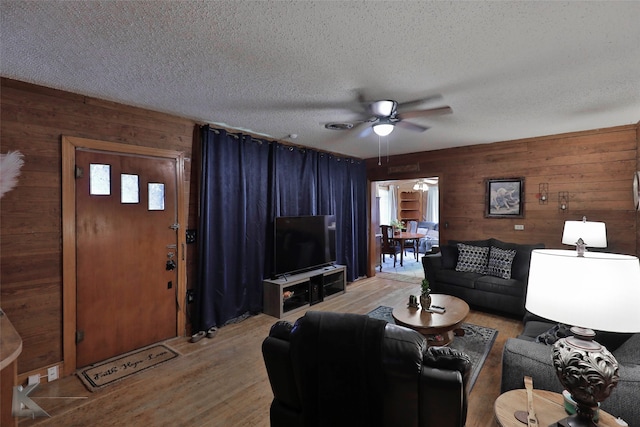 living room featuring wooden walls, ceiling fan, wood-type flooring, and a textured ceiling