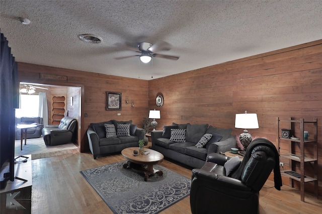 living room with wood walls, ceiling fan, light hardwood / wood-style floors, and a textured ceiling