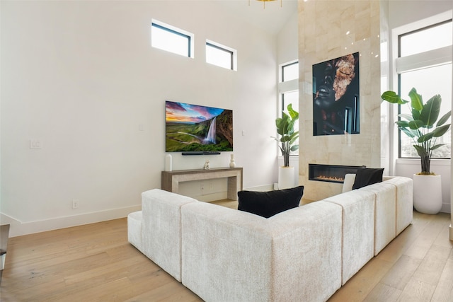 living room featuring a high ceiling, a tiled fireplace, and light wood-type flooring