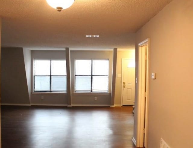 unfurnished room featuring a healthy amount of sunlight, a textured ceiling, and dark hardwood / wood-style flooring