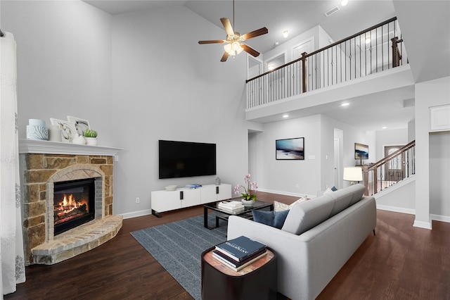 living room featuring ceiling fan, high vaulted ceiling, dark hardwood / wood-style flooring, and a stone fireplace