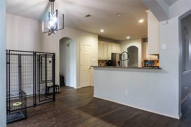 kitchen with dark wood-type flooring, kitchen peninsula, an inviting chandelier, and stainless steel fridge