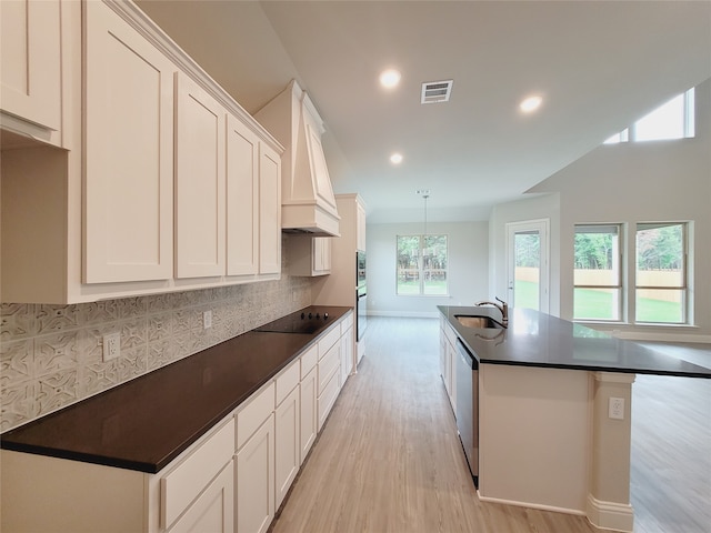 kitchen featuring tasteful backsplash, light wood-type flooring, white cabinetry, a center island with sink, and custom range hood