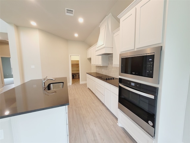 kitchen featuring oven, built in microwave, white cabinetry, backsplash, and sink