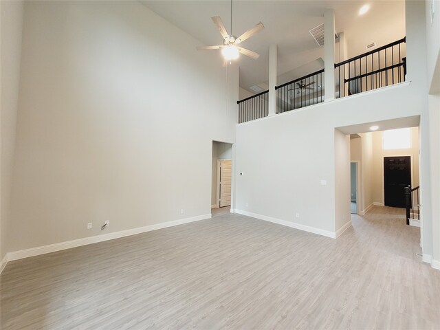 unfurnished living room with ceiling fan, a towering ceiling, and light wood-type flooring