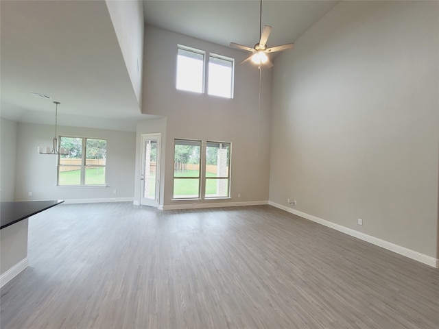 empty room featuring ceiling fan with notable chandelier, wood-type flooring, and a high ceiling