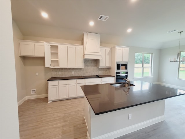 kitchen featuring custom exhaust hood, a kitchen island with sink, white cabinets, and light hardwood / wood-style floors