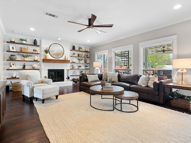 living room with ceiling fan, crown molding, a brick fireplace, and dark hardwood / wood-style floors