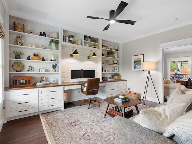 office area with built in shelves, built in desk, ceiling fan, dark wood-type flooring, and crown molding