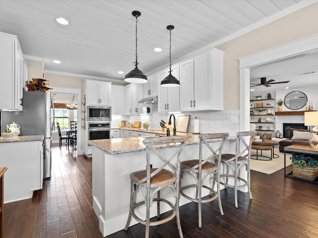 kitchen with stainless steel appliances, light stone countertops, white cabinets, decorative light fixtures, and kitchen peninsula