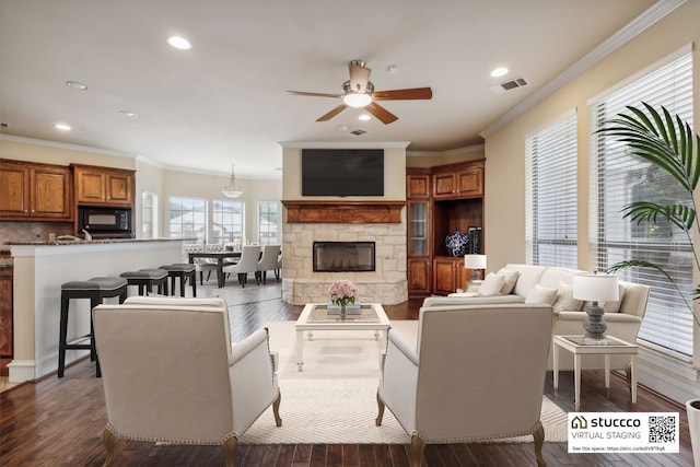 living room with ceiling fan, ornamental molding, a stone fireplace, and dark hardwood / wood-style flooring