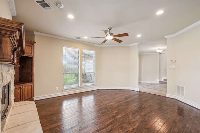 unfurnished living room with ceiling fan, dark hardwood / wood-style floors, ornamental molding, and a stone fireplace