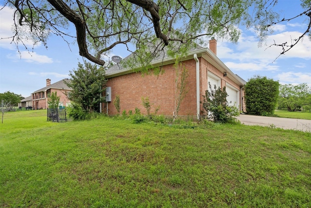 view of home's exterior with driveway, a chimney, an attached garage, a yard, and brick siding