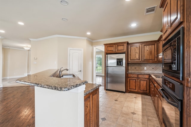 kitchen featuring a kitchen island with sink, crown molding, black appliances, sink, and light hardwood / wood-style floors