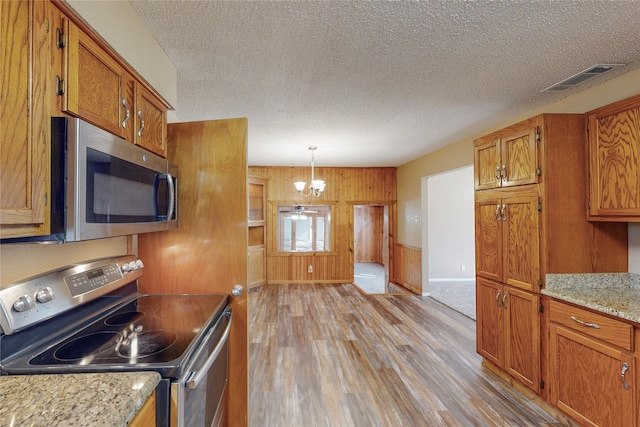 kitchen featuring light hardwood / wood-style floors, hanging light fixtures, an inviting chandelier, stainless steel appliances, and wooden walls