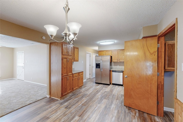 kitchen with hanging light fixtures, a textured ceiling, a chandelier, appliances with stainless steel finishes, and light hardwood / wood-style floors