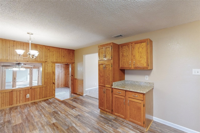 kitchen with hanging light fixtures, light hardwood / wood-style floors, ceiling fan with notable chandelier, a textured ceiling, and wooden walls