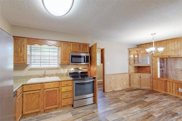 kitchen with pendant lighting, light hardwood / wood-style floors, sink, an inviting chandelier, and appliances with stainless steel finishes