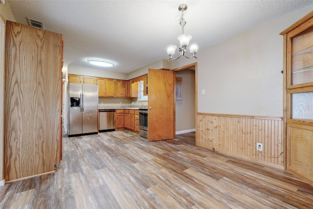 kitchen with pendant lighting, stainless steel appliances, light hardwood / wood-style floors, and a textured ceiling