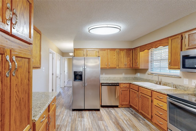 kitchen with a textured ceiling, a sink, brown cabinetry, light wood-type flooring, and stainless steel appliances
