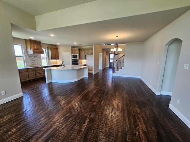 kitchen with decorative backsplash, a kitchen island with sink, dark hardwood / wood-style flooring, and a notable chandelier