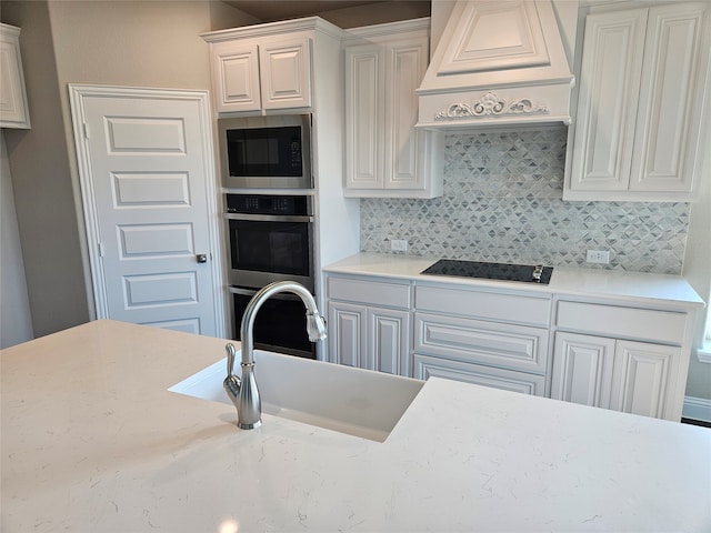 kitchen featuring sink, premium range hood, decorative backsplash, stainless steel microwave, and black electric cooktop