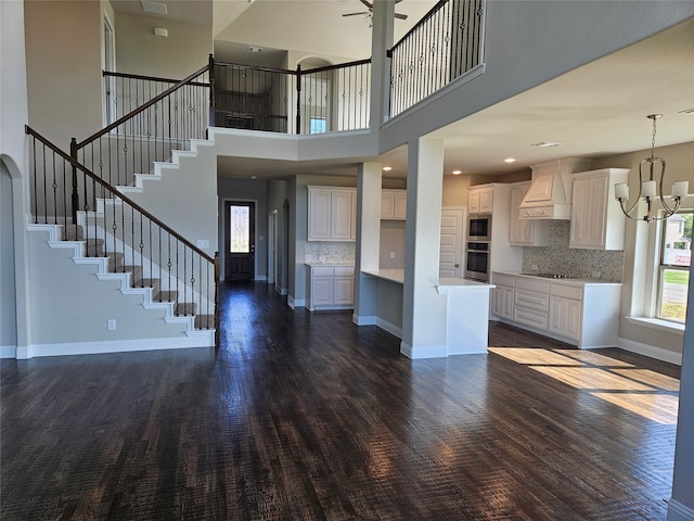 unfurnished living room with a high ceiling, dark hardwood / wood-style floors, and ceiling fan with notable chandelier