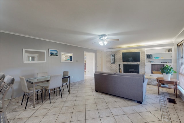 living room with a brick fireplace, ceiling fan, crown molding, light tile patterned floors, and built in shelves