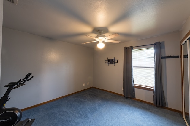 exercise area featuring a textured ceiling, ceiling fan, and dark colored carpet