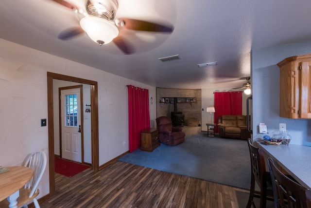 kitchen with dark wood-type flooring, ceiling fan, and a wood stove