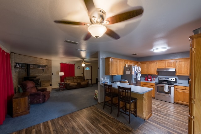 kitchen with a kitchen breakfast bar, a wood stove, appliances with stainless steel finishes, dark wood-type flooring, and ceiling fan