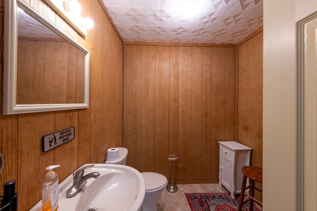 bathroom with toilet, sink, wood walls, and tile patterned floors