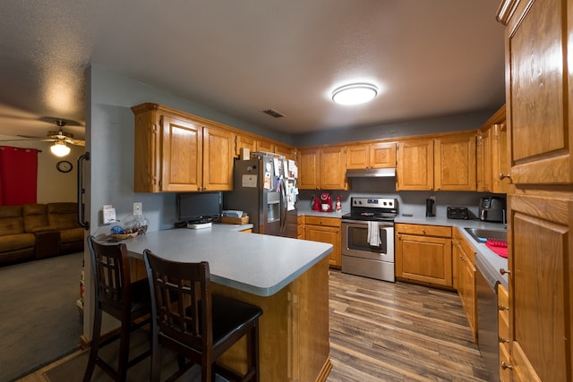 kitchen featuring a kitchen breakfast bar, stainless steel appliances, kitchen peninsula, hardwood / wood-style flooring, and ceiling fan