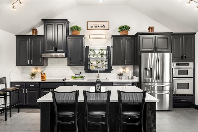 kitchen with lofted ceiling, appliances with stainless steel finishes, a center island, and track lighting