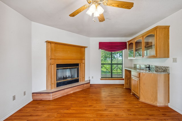 kitchen featuring wood-type flooring, ceiling fan, sink, and light stone counters