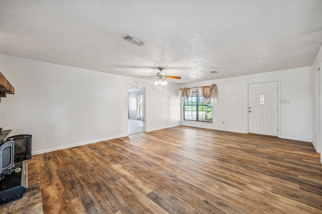 unfurnished living room with ceiling fan, hardwood / wood-style flooring, a wood stove, and a textured ceiling