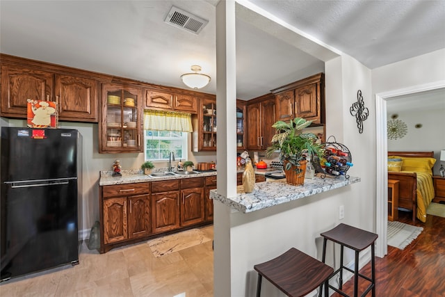 kitchen featuring light stone countertops, sink, a kitchen bar, and black fridge