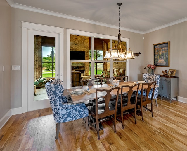 dining space featuring an inviting chandelier, light hardwood / wood-style flooring, crown molding, and a fireplace