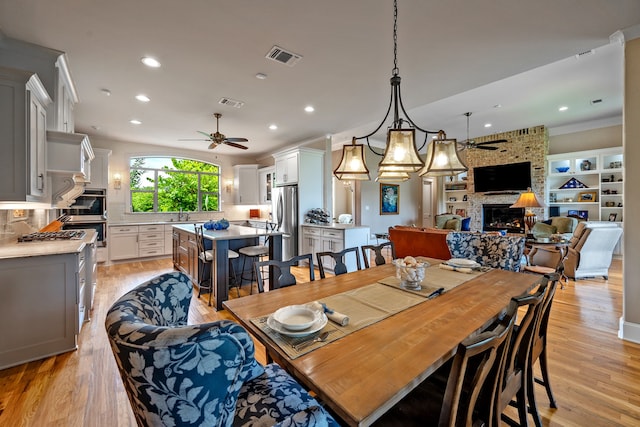 dining space featuring sink, a brick fireplace, ceiling fan with notable chandelier, crown molding, and light hardwood / wood-style floors