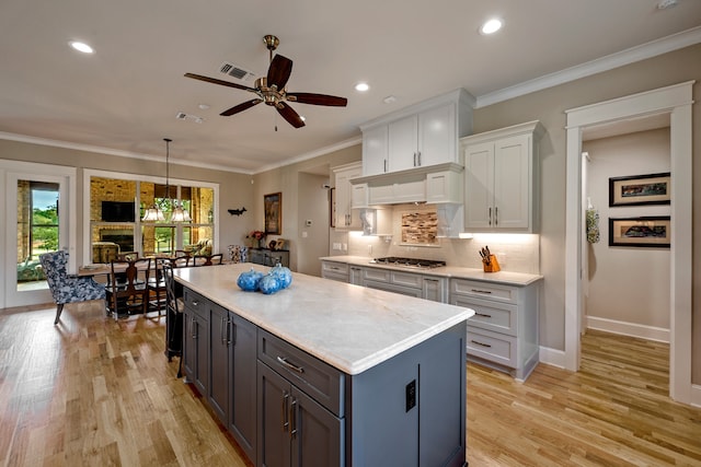 kitchen featuring a kitchen island, light hardwood / wood-style flooring, hanging light fixtures, ornamental molding, and white cabinetry