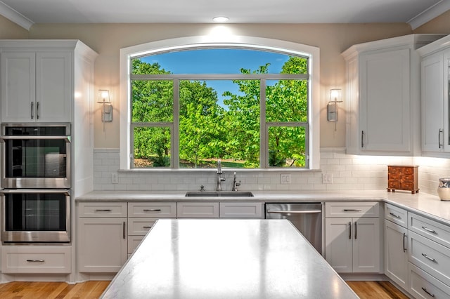 kitchen featuring decorative backsplash, stainless steel appliances, sink, white cabinetry, and light hardwood / wood-style flooring